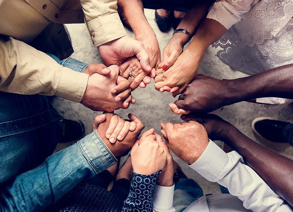 seven people's hands having different ethnicity held together in a circle