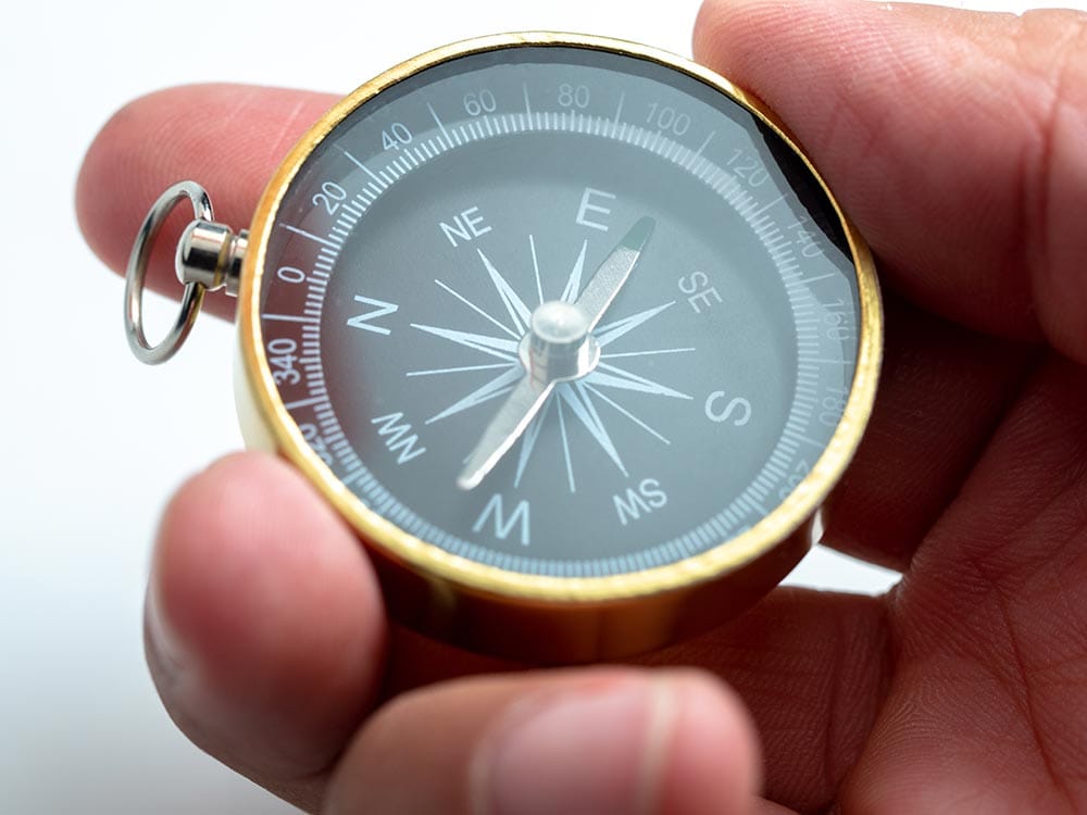Man's hand holding a gold and black compass